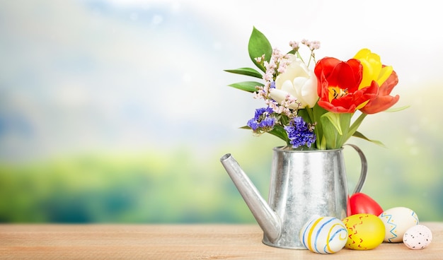 bouquet de fleurs dans un arrosoir décoratif et oeufs de Pâques sur une table en bois