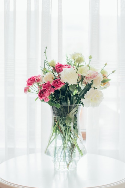 Bouquet de fleurs dans un vase transparent sur la table sur le fond de la fenêtre