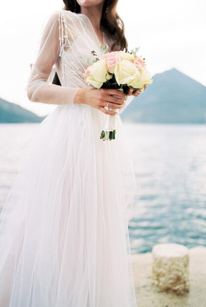 Bouquet de fleurs entre les mains de la mariée sur la jetée au bord de la mer