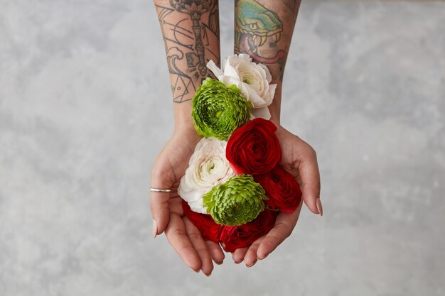 un bouquet de fleurs fraîches, une fille avec un tatouage sur les mains tenant des fleurs sur fond gris. Le concept d'une vue de dessus de carte de voeux