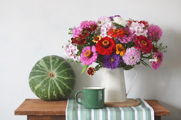 Photo un bouquet de fleurs de jardin dans une cruche et une citrouille sur une table sur un fond blanc d'été