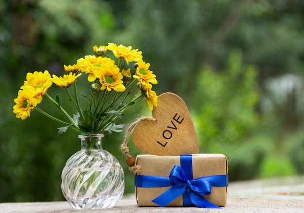 Bouquet de fleurs jaunes, cadeau et coeur en bois.