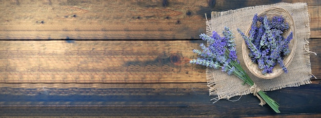 Bouquet de fleurs de lavande à côté d'un petit panier plein de pétales sur un tissu naturel sur fond de bois