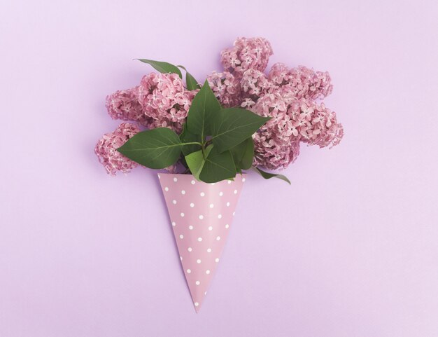 Bouquet de fleurs lilas en cône de papier sur fond violet d'en haut, à plat