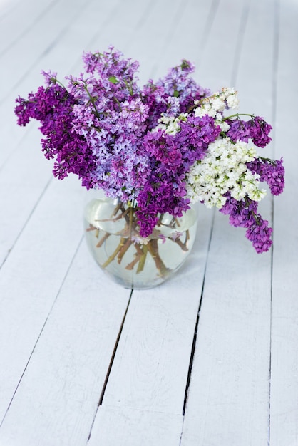 Photo un bouquet de fleurs lilas fraîches dans un vase en verre sur un plancher en bois.