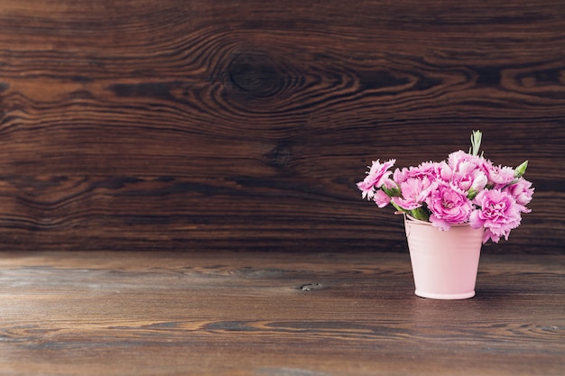 Bouquet de fleurs d'oeillets roses dans un vase sur bois. Espace vide pour le texte