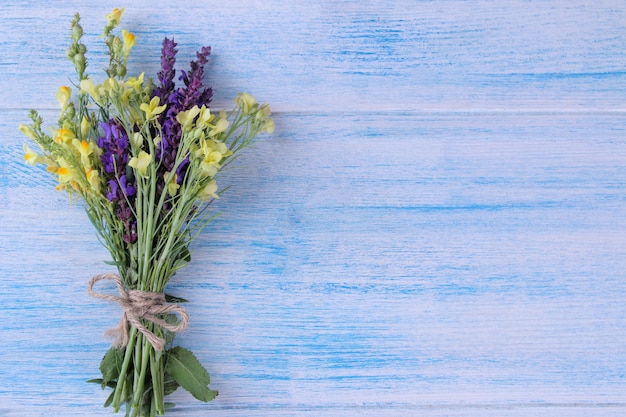 Un bouquet de fleurs sauvages jaunes et lilas sur une table en bois bleue.