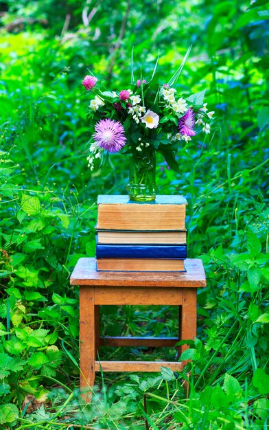 Un bouquet de fleurs de trèfle, de bleuet et de jasmin dans un vase en verre et une pile de livres