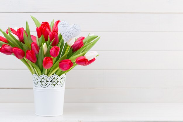 Bouquet de fleurs de tulipes rouges fraîches sur une étagère devant un mur en bois.