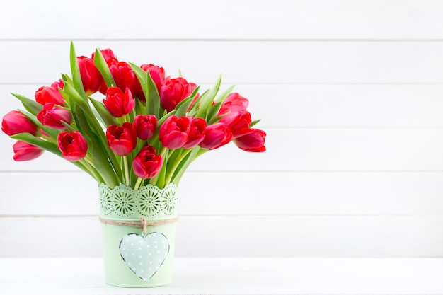 Bouquet de fleurs de tulipes rouges fraîches sur une étagère devant un mur en bois.