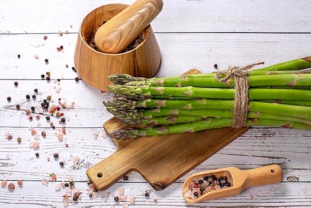 Bouquet frais cru d'asperges vertes sur planche de bois et mortier en bois avec poivre et sel