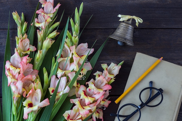 un bouquet de glaïeul, un livre, un crayon, des lunettes et une vieille cloche