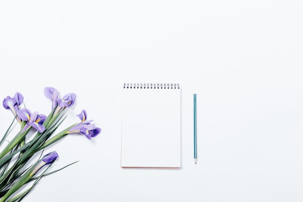 Bouquet d'iris et cahier au crayon sur une table blanche