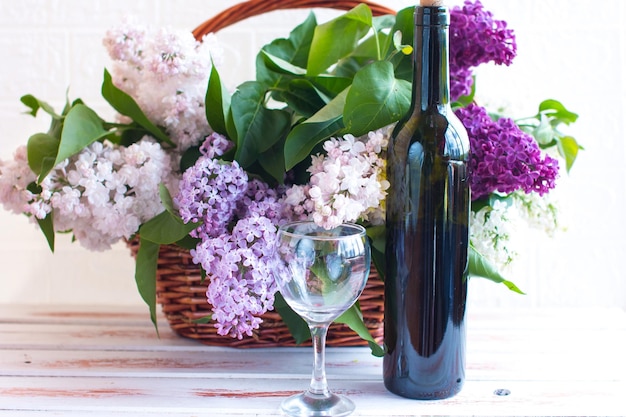 Un bouquet de lilas en fleurs dans un panier en osier Une bouteille de vin et un verre en verre