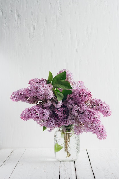 Bouquet de lilas luxuriant dans un vase sur une table en bois blanche