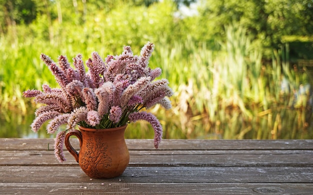 bouquet de longues inflorescences roses dans une tasse d'argile sur une surface de planche sur un arrière-plan flou