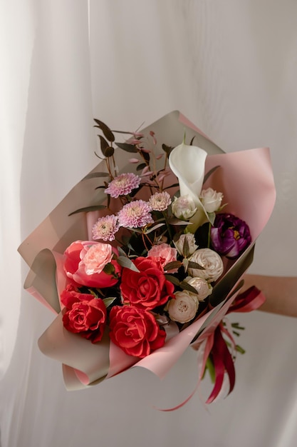Bouquet lumineux avec roses rouges callala chrysanthème roses pionoïdes dans un emballage rose