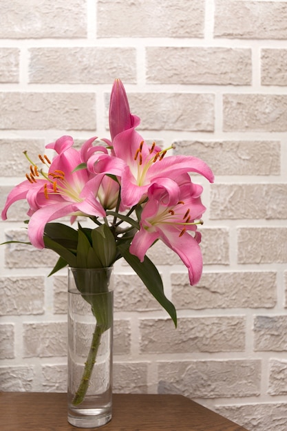 Bouquet de lys roses dans un vase en verre sur un mur de briques gris clair