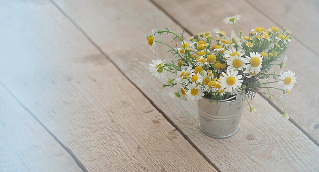 Un bouquet de marguerites blanches sur le terrain dans un petit seau en métal sur un sol en bois, une bannière horizontale avec un arrière-plan flou et un espace libre pour le texte