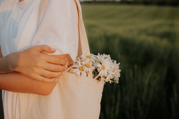 Un bouquet de marguerites des champs dans un sac blanc est suspendu à l'épaule de la fille