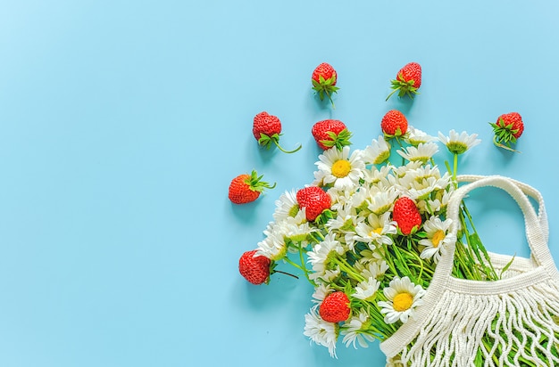 Bouquet de marguerites dans un sac en maille eco réutilisable et des fraises rouges sur fond bleu