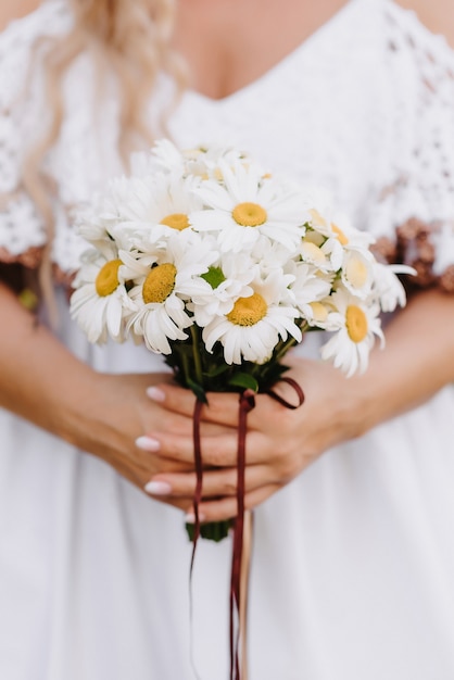 bouquet de marguerites entre les mains de la mariée sur le fond d'une robe blanche