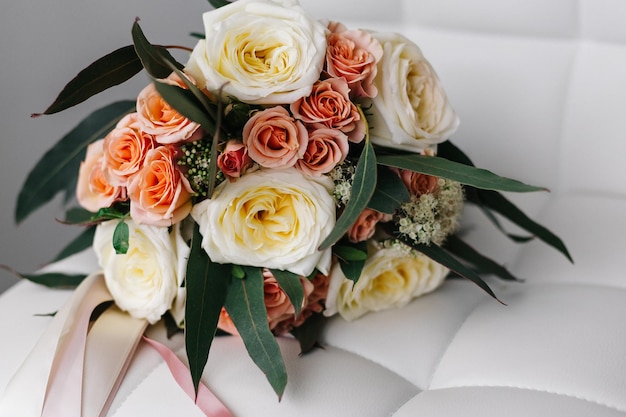 Bouquet de mariage délicat de roses beiges et roses sur une chaise en cuir blanc