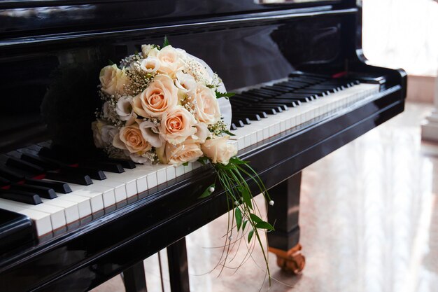 Le bouquet de mariage délicat de roses se trouve sur les touches du piano à queue