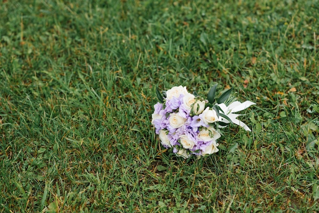 Un bouquet de mariage lilas et beige se trouve sur l'herbe verte.