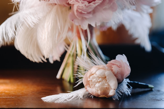 Le bouquet de mariage de la mariée de roses orné de plumes blanches et d'une boutonnière