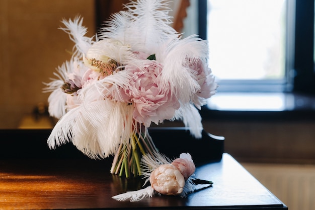 Le bouquet de mariage de la mariée de roses orné de plumes blanches et d'une boutonnière