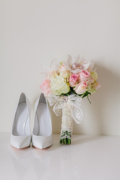 Bouquet de mariage avec des orchidées et des roses et des chaussures de mariées weddind sur fond blanc dans le style des beaux-arts