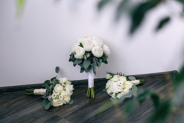 Un bouquet de mariage de roses blanches et de pivoines attachées avec un ruban blanc se trouve sur le plancher en bois