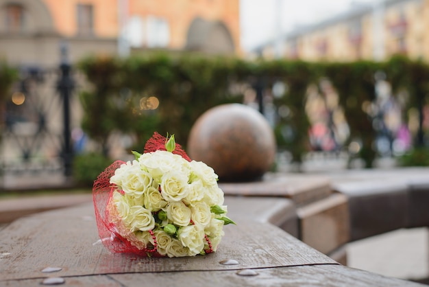 Un bouquet de mariage de roses blanches se trouve sur un banc dans la ville