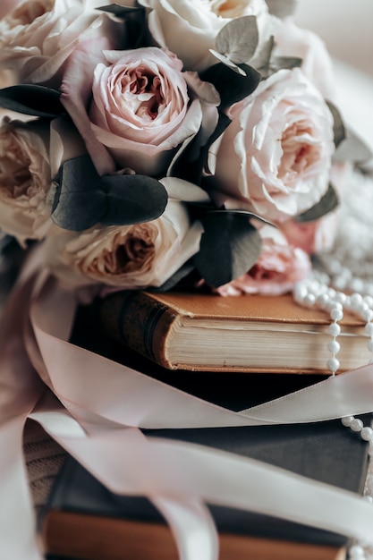 Un bouquet de mariage se trouve sur un livre ancien orange parmi les rubans de satin rose à côté de perles blanches