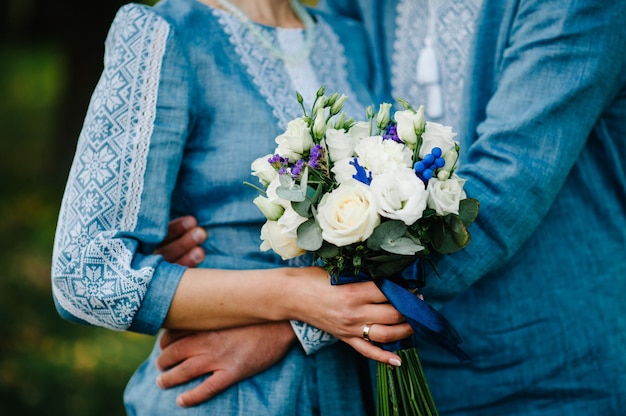 Bouquet de mariée sur l'arrière-plan élégant brides femme portant une robe brodée et le marié en chemise détient un bouquet. Cérémonie de mariage. Fermer.