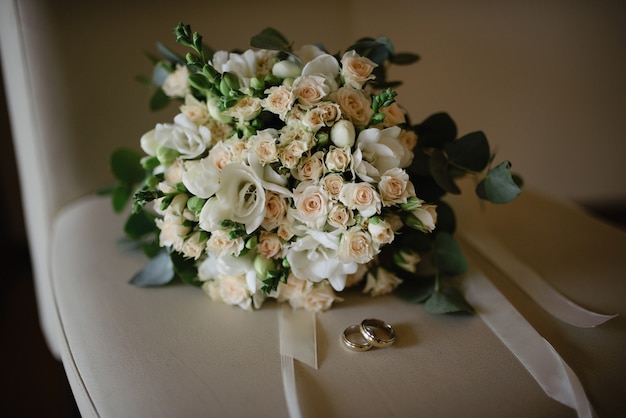 Bouquet de mariée et bagues de mariage sur une chaise beige