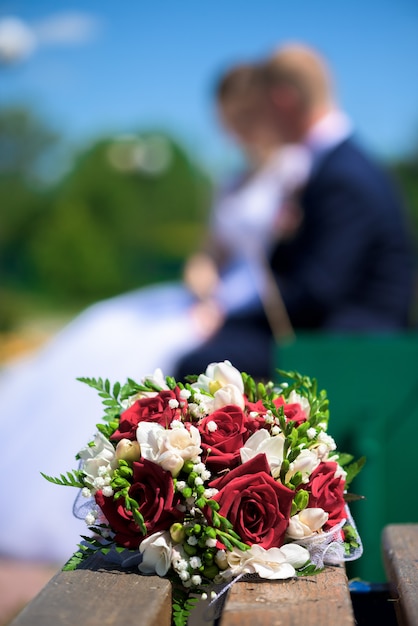 Bouquet de la mariée sur un banc sur couple d'amoureux flou