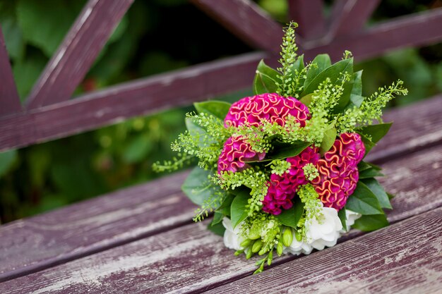 Bouquet de mariée sur le banc de jardin. Accessoire traditionnel de la mariée. Composition florale avec des fleurs de célosia rouge.
