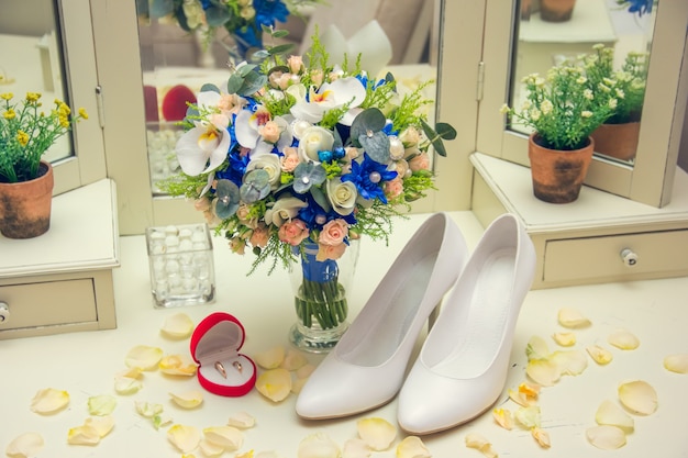 Bouquet de mariée debout dans un vase sur la table. Chaussures et bagues aux pétales de rose.