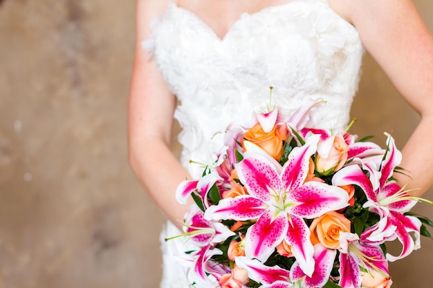 Bouquet de mariée avec des lys roses et des roses oranges.