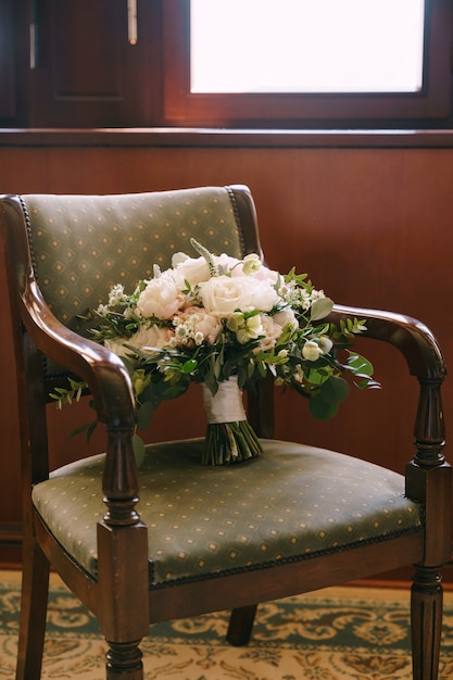 Bouquet de mariée de pivoines blanches roses véronique et branches d'eucalyptus sur un fauteuil en bois