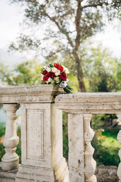 Bouquet de mariée de roses blanches et crème ornithogalum eryngium avec des rubans blancs sur la balustrade