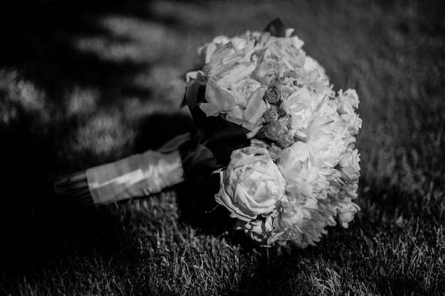 Bouquet de mariée de roses blanches, décoré de rubans de soie, allongé sur l'herbe. photographie en noir et blanc