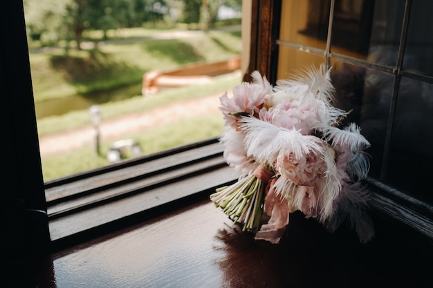 Bouquet de mariée de roses orné de plumes blanches sur le rebord de la fenêtre