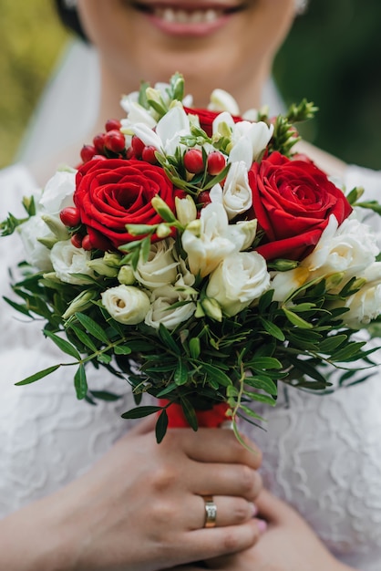 Bouquet de mariée avec des roses rouges et blanches dans les mains de la mariée