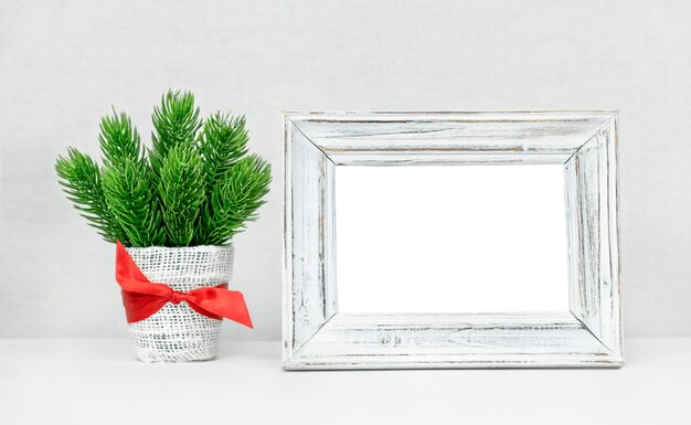 Un bouquet de Noël de brindilles de sapin dans un pot est sur la table près du cadre photo