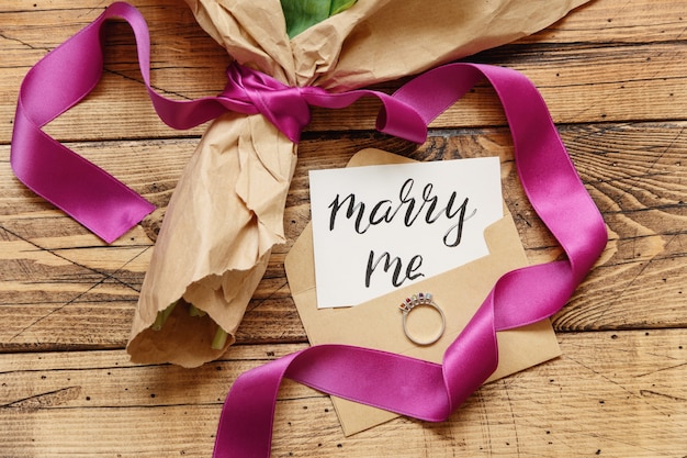 Bouquet en papier kraft avec une carte MARRY ME et anneau de proposition sur la vue de dessus de table en bois