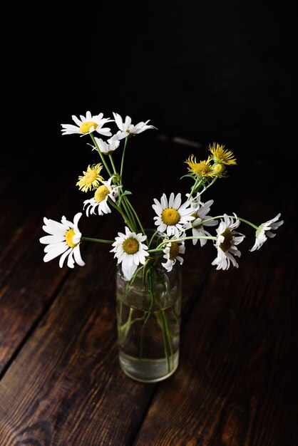 Bouquet de petites fleurs de camomille dans une bouteille sur une table en bois