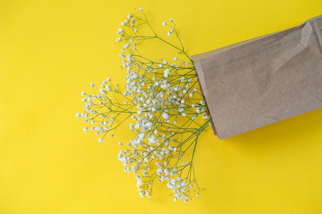 Un bouquet de petites fleurs de gypsophile dans un sac écologique sur un fond de table jaune avec un espace réservé au texte